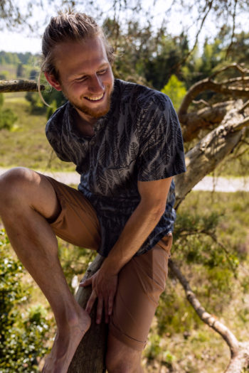 Mann lehnt sich an einen Baumstamm in einer Hose mit GOTS-Siegel.